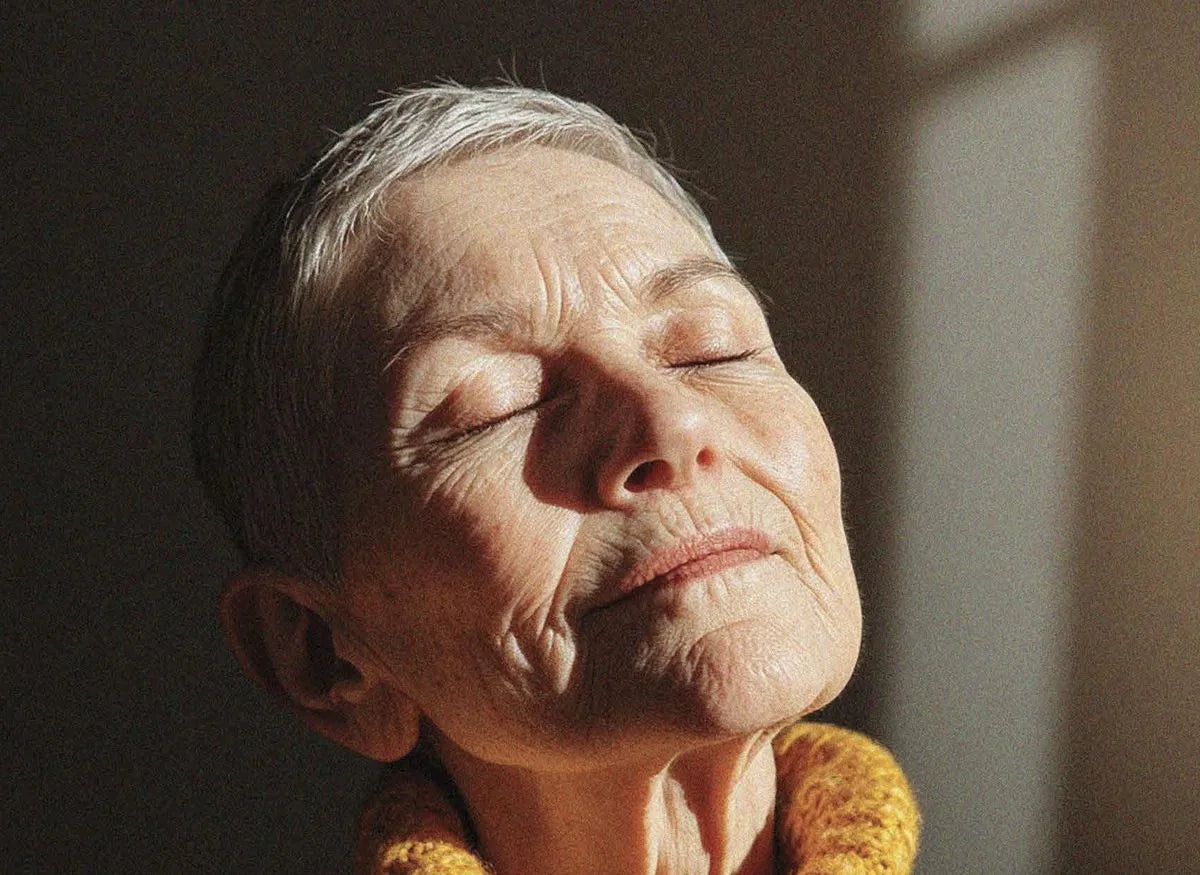 An older woman with her eyes closed, her face lit by warm sunlight